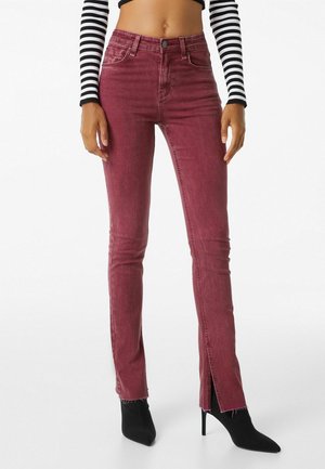 Burgundské skinny džíny s předními rozparky na lemu, se pěti kapsami a zapínáním na knoflík. Nosené s černými špičatými podpatky a pruhovaným topem.