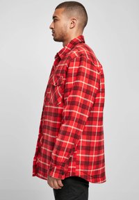 Red and black plaid shirt with long sleeves, buttoned front, and two chest pockets. Made of soft fabric with a relaxed fit.