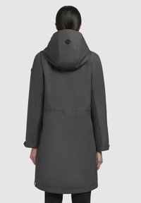 Veste à capuche gris foncé avec une taille cintrée, des manches longues et une texture lisse. Présente un logo sur la capuche et un design minimaliste.