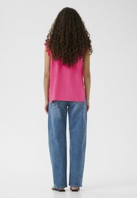 Top fucsia senza maniche con dettagli in pizzo, abbinato a jeans in denim blu a vita alta e gamba ampia. La texture appare morbida e liscia.