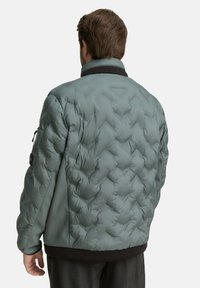 Puchowa kurtka w jasnym zielonym kolorze z pikowanym wzorem, z czarnym kołnierzem i mankietami oraz bocznymi kieszeniami na zamek dla funkcjonalności.