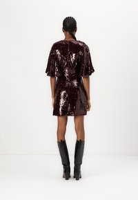 Robe en sequins bordeaux avec des manches courtes et flottantes et une fermeture éclaire dans le dos, associée à des bottes noires à talons hauts jusqu'aux genoux. Texture lisse et brillante.