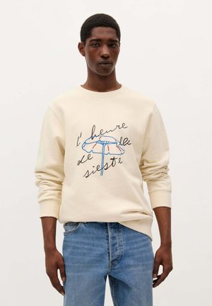 Sudadera beige con cuello redondo que presenta un gráfico colorido de un paraguas y el texto "l'heure de la sieste" en letras negras y azules.