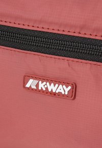 K-Way táska tompa piros anyagból, finom rácsos textúrával, fekete cipzárral és a felületre varrt fehér logó címkével.