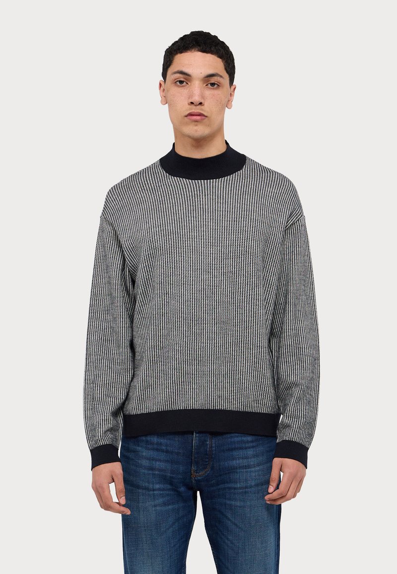 Maglione a righe bianche e nere con colletto alto a coste, maniche lunghe e vestibilità strutturata. Indossato con jeans in denim blu.