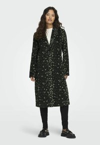 Lungo cappotto nero con motivo leopardato verde, chiusura a bottoni, colletto a punta e maniche lunghe, abbinato a pantaloni e scarpe neri.