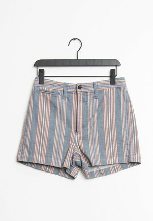 Blå shorts med lodrette orange, hvide og lilla striber hængende på en sort klemmebøjle mod en hvid baggrund.