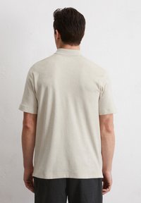 Beige polo shirt met korte mouwen, gemaakt van een zachte, gestructureerde stof, met een standaard kraag en een rechte onderkant, gedragen met donkere broek.
