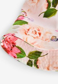 Ziedu izeju cepure mīkstā audumā, ar gaiši rozā fona, rotāta ar dzīvīgām rozēm un lapu rakstiem. Izliektā mala ar šuvju akcentiem.