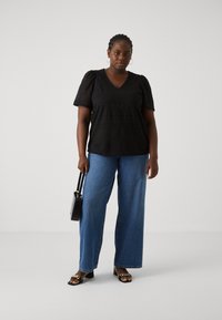 Black short-sleeved top with textured patterns, V-neck design, paired with wide-leg blue denim jeans. Model holding a small black handbag.