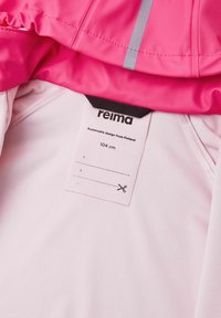 Interno di giacca rosa con foderatura bianca. Presenta un'etichetta di cura che indica la taglia 104 cm e "design sostenibile dalla Finlandia."