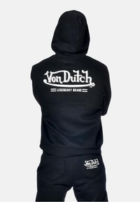 Sweat à capuche noir avec le logo blanc "Von Dutch Legendary Brand" au dos. Présente une coupe décontractée et est fabriqué en tissu doux.