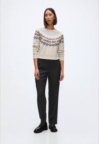 Heled beeži sviiter, millel on kaeluse ümber värvilised geomeetrilised mustrid, kombineeritud tumesiniste pükstega ja mustade tükkjalatsitega.