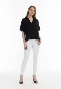Sort løstsiddende bluse med krave, kort ærmer og V-halsdesign, parret med hvide skinny jeans og sorte højhælede sko.