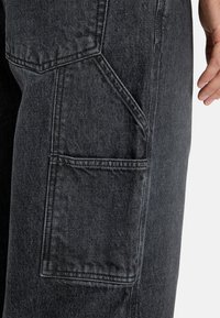 Czarne dżinsowe spodnie cargo z boczną kieszenią, charakteryzujące się teksturowanym materiałem, prostym krojem nogawki oraz kontrastowymi stębnowaniami.