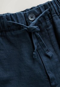 Primer plano de pantalones texturizados azul marino con cintura elástica, cordón ajustable y un cierre con un único botón negro.