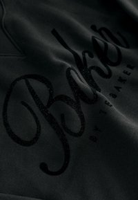 Primer plano de una tela negra con "Picos" texturizados y brillantes en negro, y el texto más pequeño "Day Breaker" impreso sobre ella.