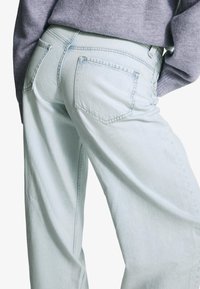 Lichtblauwe denim jeans met een ontspannen pasvorm, voorzien van achterzakken en een subtiele textuur. De tailleband toont een klassiek ontwerpdetail.