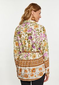 Blusa stampata floreale con sfondo crema, arricchita da fiori arancioni e viola. Presenta una vita con cinturino e maniche lunghe.
