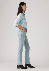 Šviesiai mėlynas džinsinis marškinis su dviem krūtinės kišenėmis, derinamas su šviesiai plovtais tiesiais džinsais ir juodais aulinukais. Lygus tekstūra ir pritaikytas kirpimas.