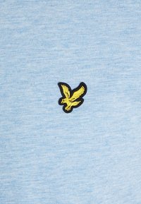 Světle modré bavlněné tričko s žlutým vyšitým logem orla, obrysem v černé barvě, na levé straně hrudi.