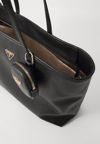 Svart skinn toteveske med doble håndtak, gullfarget tilbehør og en avtagbar rund glidelåspose. Inni har den en brun stoffforing med logoer.