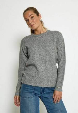 Pull en tricot gris avec un col rond, des poignets et un ourlet côtelés. Texture douce et coupe décontractée, associé à un jean bleu.
