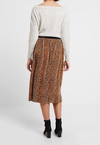 Jersey de punto grueso, con los hombros al descubierto, en gris claro, combinado con una falda de leopardo marrón a la altura de la rodilla, que presenta una cinturilla negra y botas hasta el tobillo.