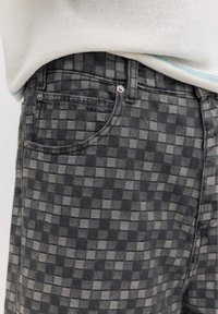 Pantalon à carreaux noir et gris porté avec un pull en maille blanc avec une bordure bleu clair en bas.