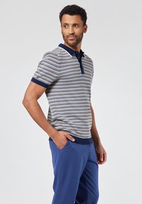 Polo de punto con un patrón de diamantes multicolor, con cuello y puños en navy, combinado con pantalones azules con cinturilla elástica y bolsillos laterales.