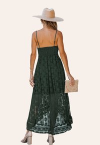Donkergroene kanten maxi-jurk met verstelbare spaghetti-halsbandjes, textuur bovenlichaam, bloemmotieven en een doorschijnende onderlaag. Gemaakt met een strooien clutch.