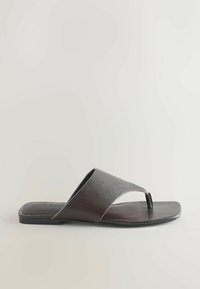 Sandale à lanière en cuir marron foncé avec une bride large, un bout carré et une semelle plate sur un fond clair uni.