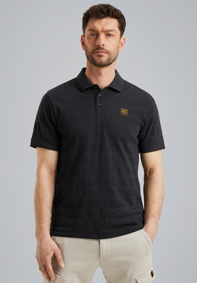 Zwarte polo met een subtiele gestreepte structuur, voorzien van een drieknoopsluiting en een klein rechthoekig logo-patch op de borst.