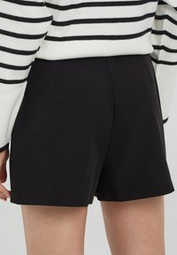 Pantaloni corti neri a vita alta con una texture liscia e design minimale, abbinati a un maglione a righe bianche e nere.