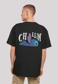 Black cotton t-shirt featuring a graphic of Stitch lying down, with the word "CHILLIN" in bold white text above in a playful font.