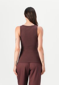 Top en coton lisse ajusté marron, avec un col rond et de larges bretelles, associé à un pantalon ample assorti.