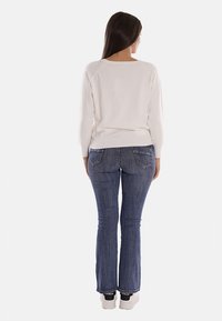 Maglione beige chiaro con scollo rotondo e maniche lunghe, abbinato a jeans a campana di denim blu scuro e scarpe bianche con dettagli neri.
