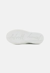 Suela de zapato de goma blanca con una textura suave. Presenta un logo en cursiva y forma redondeada. La suela muestra un ligero desgaste y está limpia en general.