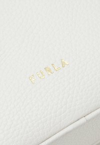 Biała skórzana portmonetka z teksturowaną powierzchnią. Złote logo "FURLA" wytłoczone z przodu. Prosty, prostokątny kształt z zaokrąglonymi krawędziami.