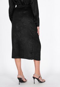 Vestido midi de satén negro con textura suave, mangas largas y detalle de cintura anudada. Combinado con sandalias negras de tacón con detalles plateados.