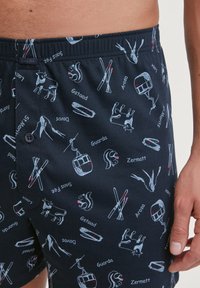 Blauwe katoenen shorts met een gemengd patroon van ski-gerelateerde graphics en Zwitserse plaatsnamen, met een elastische tailleband en een functionele knoop.