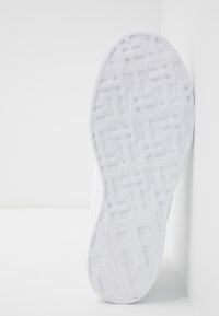 Weiße Sneaker-Sohle mit einem strukturierten Muster und geometrischen Formen. Branding im Fersenbereich sichtbar, gefertigt aus einem strapazierfähigen Material.