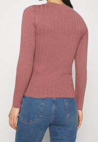Taillierter gerippter Pullover in Puderrosé, mit langen Ärmeln und rundem Halsausschnitt, kombiniert mit hoch taillierten blauen Jeans.