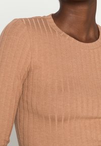 Top lungo a maniche ribatte con collo rotondo e texture verticale; tessuto morbido e elasticizzato con silhouette aderente.