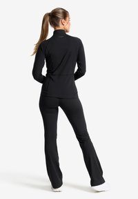 Svart långärmad träningsöverdel med en hög krage, ihop med svarta utsvängda byxor. Tillverkad av elastiskt tyg med en figurnära design.