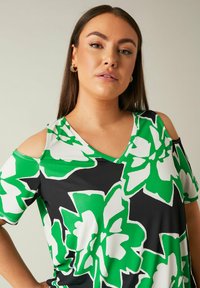 Top nero con grandi stampe floreali verdi e bianche, caratterizzato da un design a spalle scoperte, scollatura a V e una morbida texture di tessuto liscia.