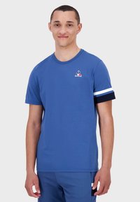 Heren blauwe katoenen t-shirt met korte mouwen, featuring een ronde halslijn en contrasterende marineblauwe en witte gestreepte accenten op de mouwen. Logo-detail op de borst.