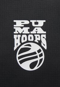 Fond en tissu noir avec le texte blanc "PUMA HOOPS" et un graphique stylisé de basketball avec des lignes courbes et des détails circulaires.