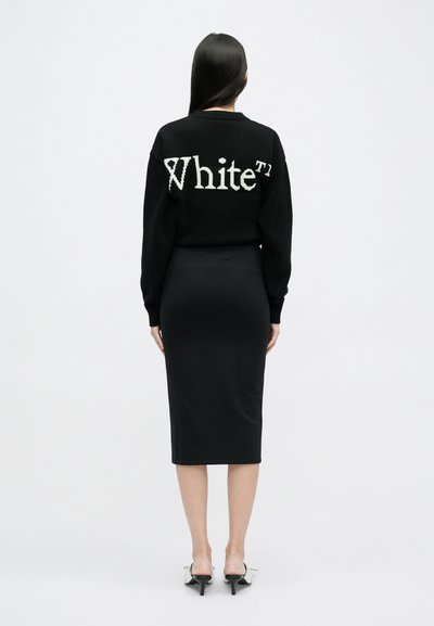 Czarny sweter z dzianiny z dużym białym napisem "White" na plecach, w zestawie z dopasowaną czarną spódnicą midi i białymi sandałami na obcasie.