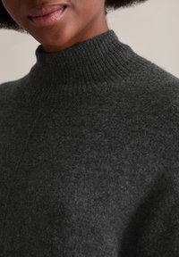 Dunkelgrauer, gerippter Rollkragenpullover aus weichem, strukturiertem Material. Eine Nahaufnahme hebt den Kragen und die aufwendigen Strickdetails hervor.